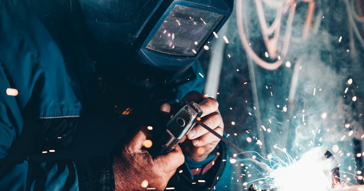 Welder wearing a helmet MIG welding a steel part, with sparks